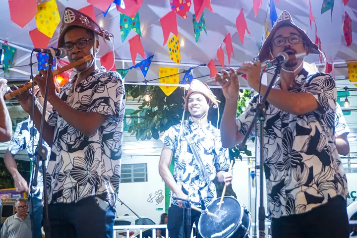 Banda de forró com pífano e zabumba tocando sob bandeirinhas coloridas