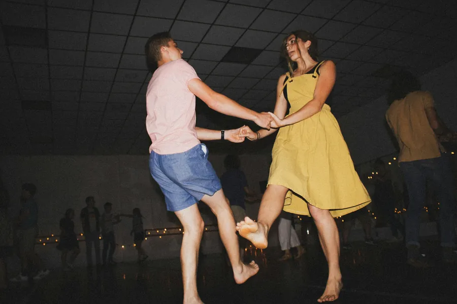 Casal descalço dançando de mãos dadas num salão à meia-luz