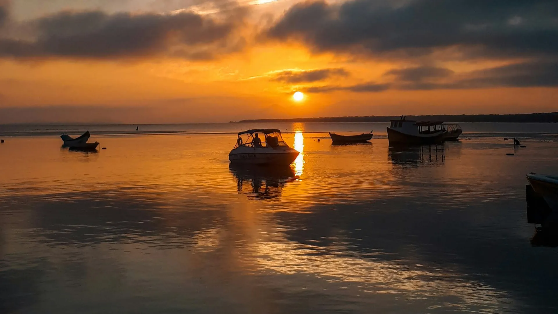 Pôr do sol alaranjado sobre a baía da Ilha do Mel, com barcos parados na água
