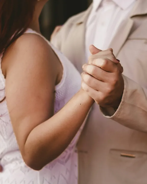 Mãos de um casal entrelaçadas na postura de dança a dois